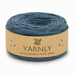 A roll of Yarnly faux leather t-shirt yarn in a muted slate blue color, wrapped in a kraft paper band with the brand name clearly visible.
